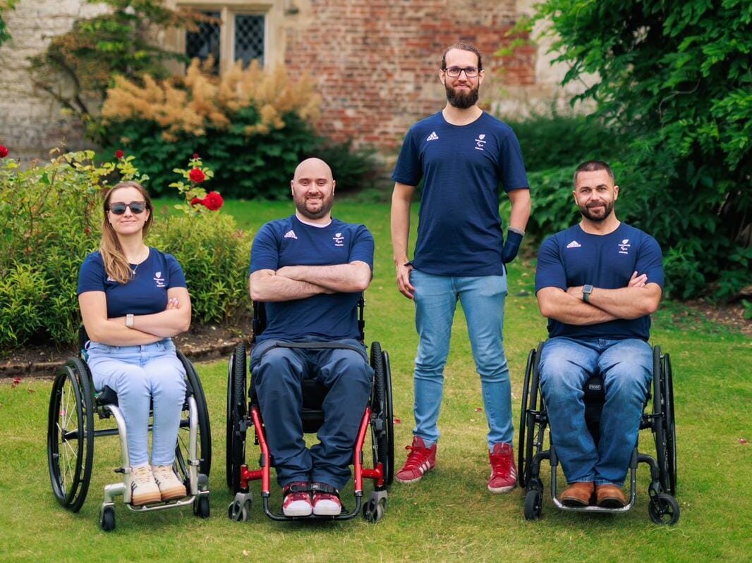 Four Paralympic athletes pose for a photo in a garden. Three are using wheelchairs whilst one stands.