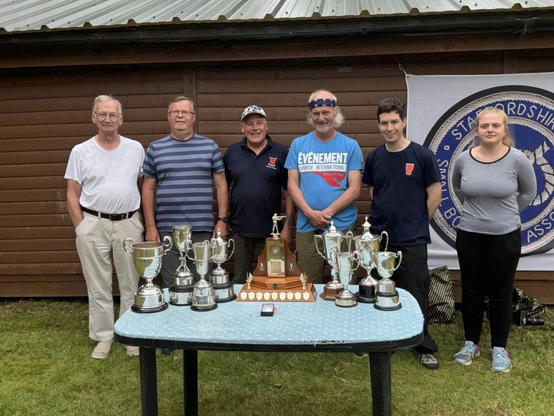 A group of people stand behind a table laden with trophies that they have won at a target rifle shooting competition in the United Kingdom.