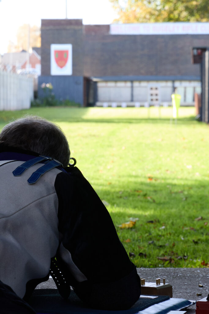 A man aims a target rifle on a 100yard range. He is ling on his front in the prone position.